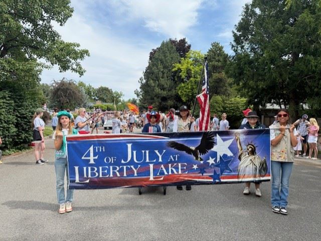 Image of in a parade kids holding a banner that says 4th of July at Liberty Lake.